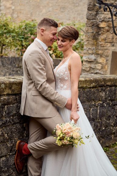 Braut und Bräutigam posieren romantisch vor einer Steinterrasse mit Blumenstrauß.