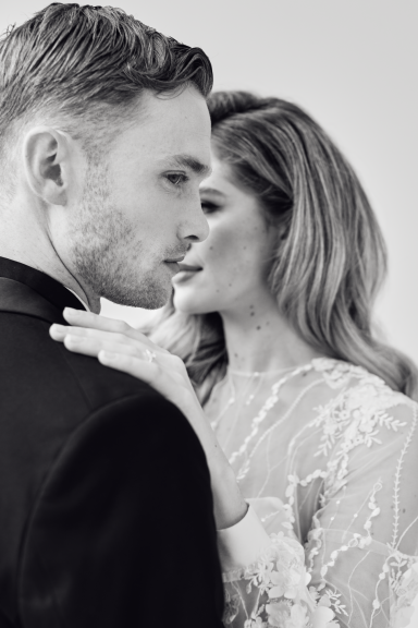 Ein Paar in eleganter Kleidung, eng umschlungen und intim lächelnd.