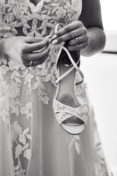 Händedetails einer Person, die einen eleganten Brautschuh hält.