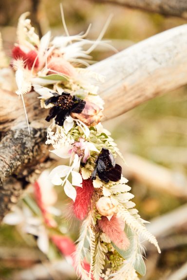 Blumenkranz mit bunten Blüten und grünem Blattwerk an einem Zweig.
