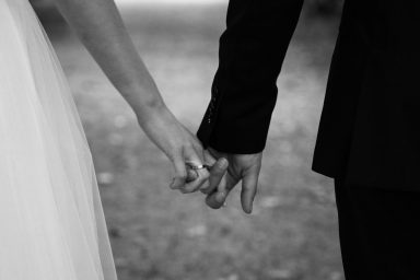 Händchen haltendes Brautpaar auf einem romantischen Weg.