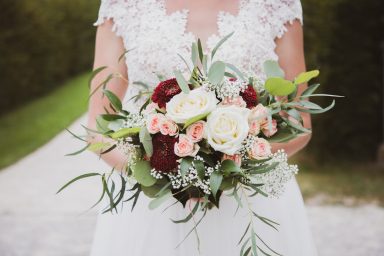 Braut hält einen bunten Blumenstrauß mit Rosen und Grünpflanzen.