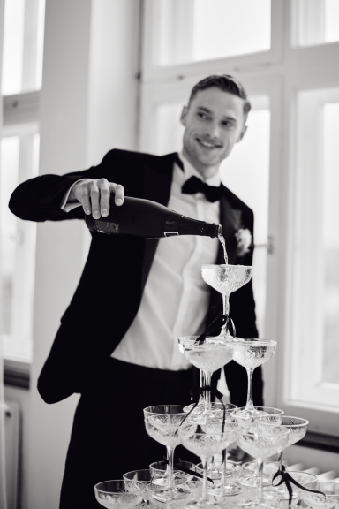 Ein Mann im Anzug schenkt Champagner in eine Gläser-Turm.