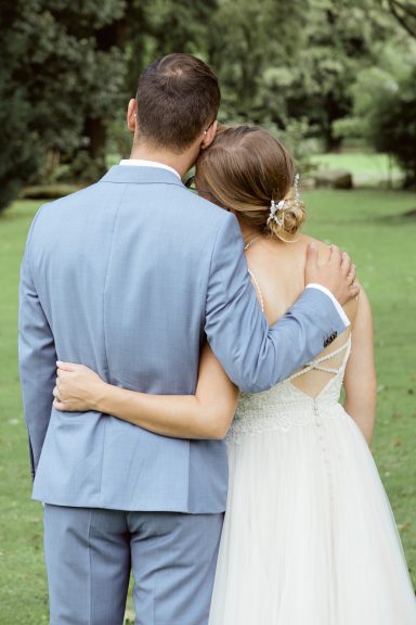 Braut und Bräutigam von hinten, umarmend in einer grünen Landschaft.