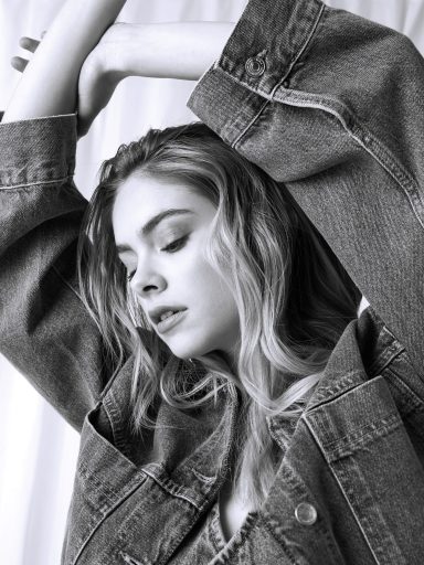 Frau mit langen, lockigen Haaren in Oversized-Jeansjacke, nachdenklicher Ausdruck.