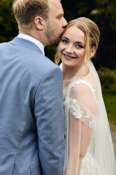 Braut und Bräutigam posieren fröhlich im Freien, sie lächeln sich an.