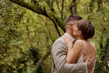 Paar umarmt sich innig in einer grünen, bewaldeten Umgebung.