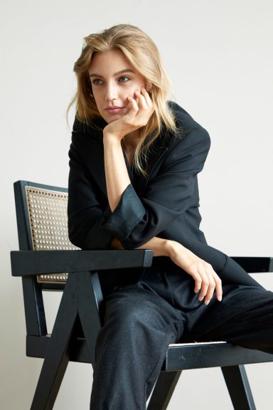 Junge Frau in schwarzem Anzug sitzt nachdenklich auf einem Stuhl.