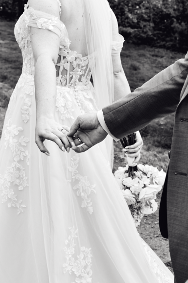 Braut und Bräutigam halten Händchen, die Braut trägt ein elegantes Hochzeitskleid.