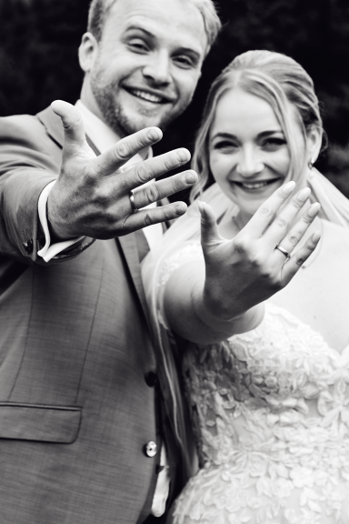 Braut und Bräutigam lächeln und zeigen ihre Ringe, umgeben von einem romantischen Ambiente.