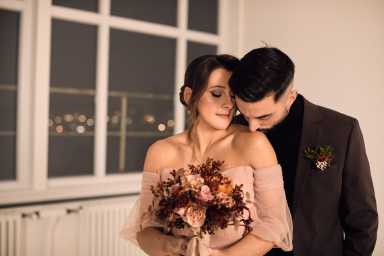 Paar in eleganter Kleidung mit Brautstrauß, romantische Stimmung im Hintergrund.