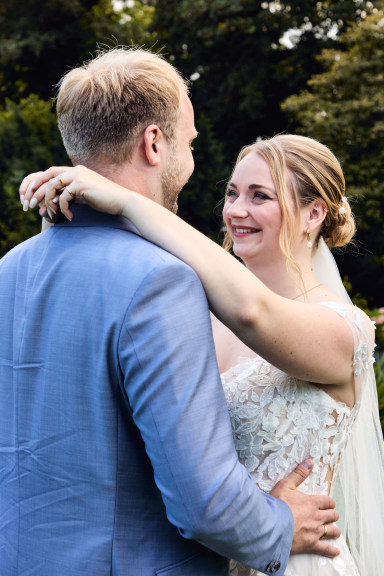 Ein Brautpaar umarmt sich glücklich im Freien, umgeben von Natur.