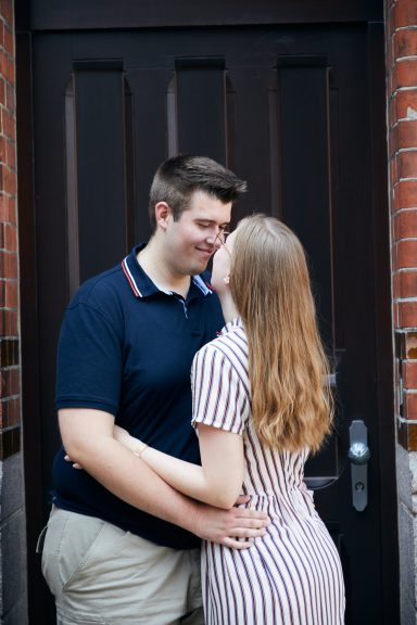 Paar umarmt sich vor einer braunen Tür, beide lächeln sich an.