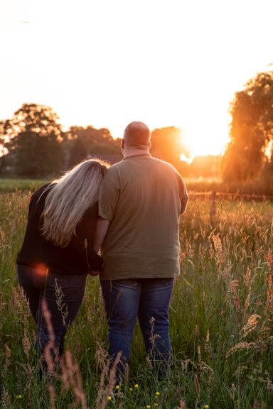 Ein Paar hält sich in einer Wiese bei Sonnenuntergang an den Händen.
