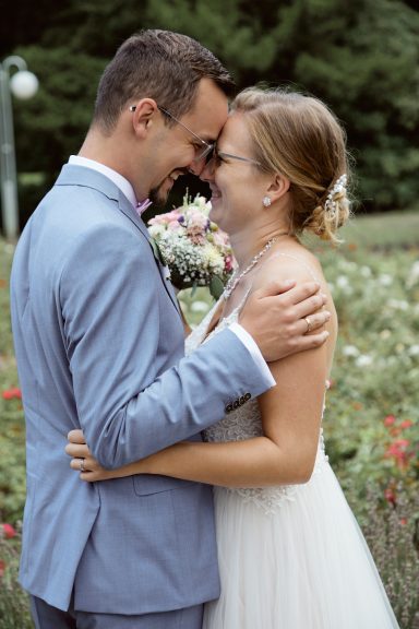 Paar umarmt sich liebevoll in blühendem Garten, beide lächeln glücklich.