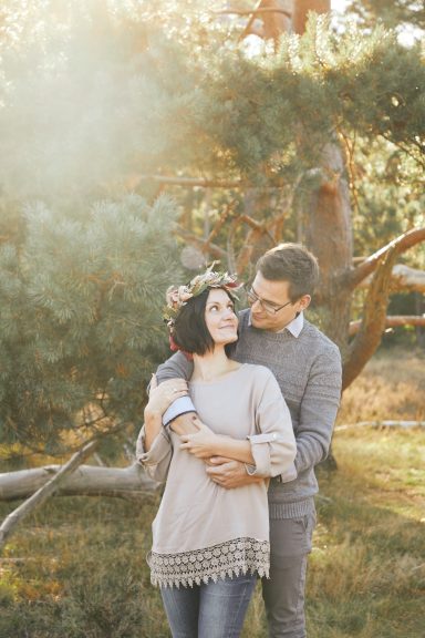 Paar umarmt sich lächelnd in einem sonnendurchfluteten Wald.